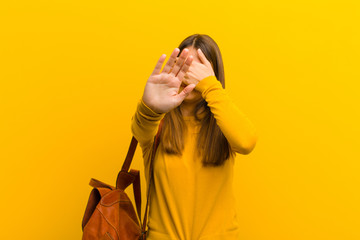 young pretty woman covering face with hand and putting other hand up front to stop camera, refusing...