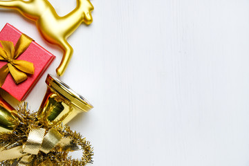 Golden Christmas reindeer, bells with tinsel and red gift on white wooden background with copy space.