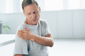 handsome man in t-shirt feeling pain in shoulder in apartment
