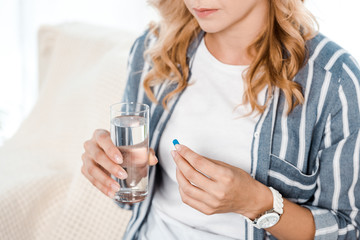 cropped view of woman holding glass with water and pill