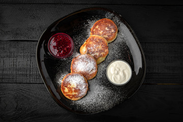 Lush tasty curd cheesecakes with raspberry jam in a dark plate on black boards. Hearty Nutritious Healthy Breakfast
