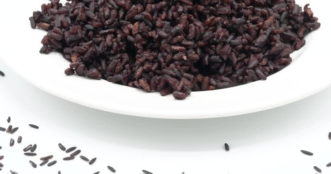 Steamed Riceberry rice on plate rotating on white background, organic rice from Thailand.