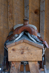Worn comfortable leather western saddle on a wood saddle stand against a rustic wood wall