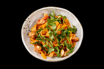 Closeup plate of tagliatelle pasta with shrimps, tomatoes and arugula isolated at black background.