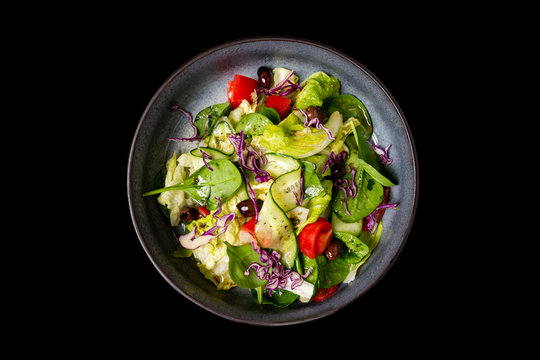 Top view image of healthy vegan vegetable salad with tomatoes, cucumbers, olives and salad mix isolated at black background.