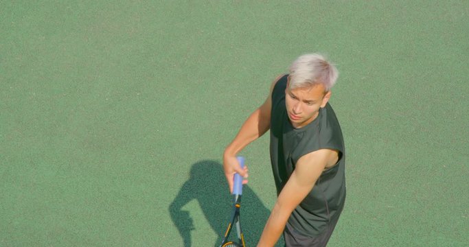 A mixed race tennis player with platinum hair serves in slow motion.