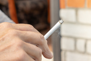 Man holding a lighted cigarette in fingers with a lot of ashes, bad habbits and nicotine addiction...