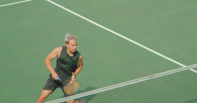 A Tennis player runs across court at the net and volleys in slow motion.