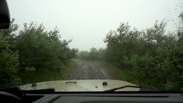 Pov shot drving on a dirt road on a rainy and stormy day in Alaska.