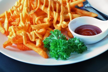 Selective focus of golden french fries with cheese and a spoon of catchup on white plate.