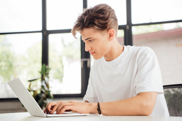 focused teen boy in white t-shirt using laptop at home