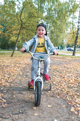 little boy, child 3-5 years old, smiles happy, laughs, rides bicycle, on summer spring autumn day in a city park, keeps his balance, rests on weekends, learns to ride bicycle training and dexterity.