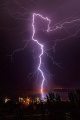 Fototapeta na wymiar Night lightning strikes the pier on the opposite bank of the river