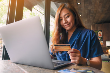 A beautiful asian woman holding credit cards while using laptop computer