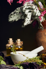 white mortar with pestle near bottles and vase with fresh flowers on wooden surface isolated on black