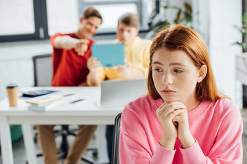 sad pensive girl and classmates laughing at her in school