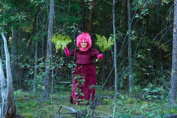 A young witch in purple clothes performs a magical ritual with a fern in the forest.