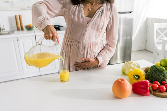 cropped view of pregnant woman pouring orange juice in glass near vegetables - Powered by Adobe