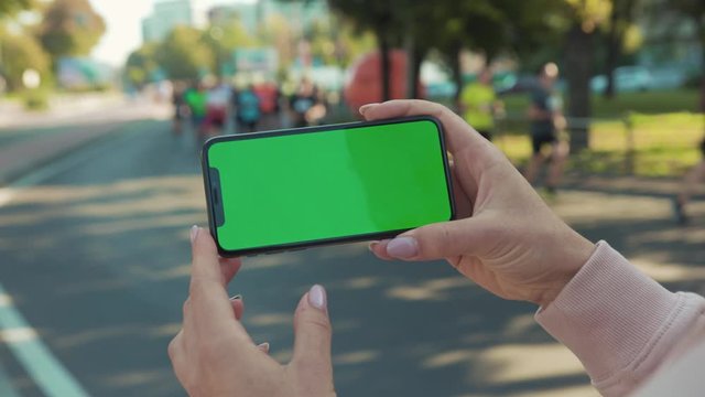  Close up of woman hands holding and touching phone with green screen horizontal in the street people crosswalk background internet technology business message slow motion