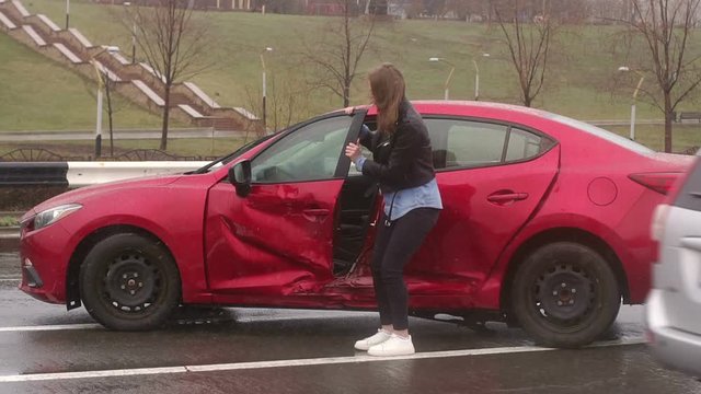 The girl slowly gets out of the car which had just crashed, she's in shock and she's scared. The girl flew into a pole at the speed of the car in the rain or snow. Slow motion.