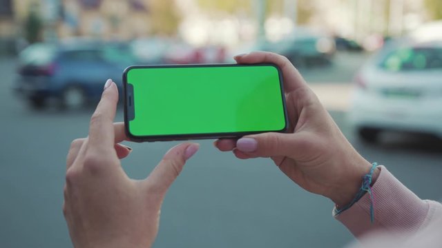  Close up of woman hands holding and touching phone with green screen horizontal in the street people crosswalk background internet technology business message slow motion
