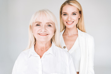 smiling blonde grandmother and granddaughter together in total white outfits isolated on grey