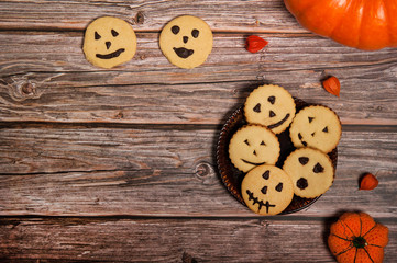 Homemade cakes for Halloween. Orange pumpkins and physalis, cookies with scary smiles on a wooden background. Free space for your text.