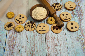 Homemade cakes for Halloween. Cornmeal, rolling pin, baking paper, cookies with spiders, bats, pumpkins, scary smiles, cobwebs on a light blue wooden background.