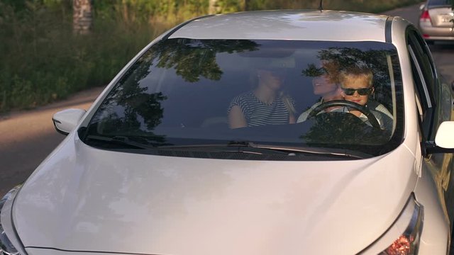 Young parents with a young son sitting in the car behind the wheel and look at the camera on an empty road in the woods. Slow motion. Family with son travels by car.