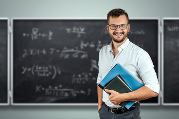 Portrait of a young male teacher on the background of the school blackboard. Teacher's Day...