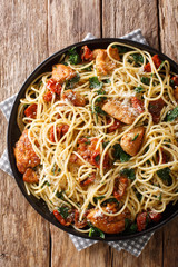 Tasty spaghetti with fried chicken, dried tomatoes and spinach close-up on a plate. Vertical top view