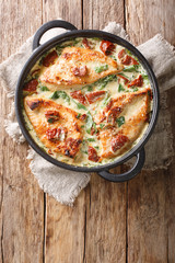 Tasty chicken fillet with sun-dried tomatoes and spinach in cheese sauce close-up in a pan. Vertical top view