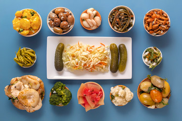 Fermented products cabbage, peppers, pickles, tomatoes, mushrooms, zucchini, garlic on a blue table. Top view