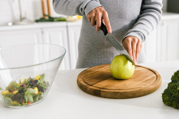 cropped view of girl holding knife near green whole apple
