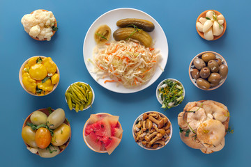 Fermented products cabbage, peppers, pickles, tomatoes, mushrooms, zucchini, garlic on a blue table. Top view