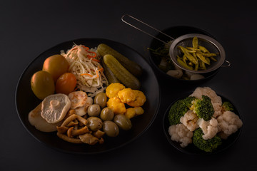 Fermented foods cabbage, peppers, pickles, tomatoes, mushrooms, zucchini, garlic in a large wooden dish on a dark table with spices for salting. Low key.