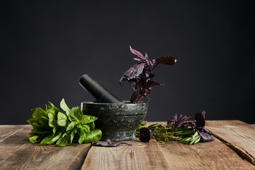 mortar with pestle near fresh green and purple basil on wooden table isolated on black