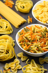 Italian food ingredients - pasta, vegetables, mushrooms, bacon, eggs, olives. Flat lay on dark wooden background
