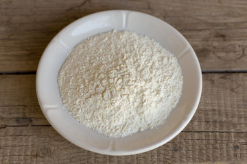 flour in a plate on antique, dark, wooden background