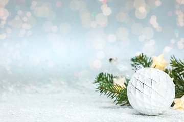 Fototapeta na wymiar beautiful christmas snowy background with green fir tree branch, white glass ball and glowing star lights