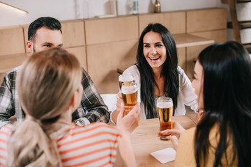 back view of young women clinking glasses of light beer with friends in pub
