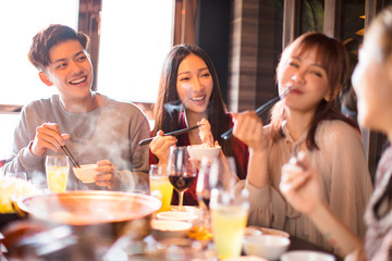 happy young friends enjoy dinner in hot pot restaurant
