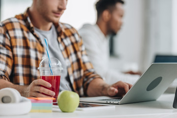 cropped view of programmer working at laptop while sitting near african american colleague