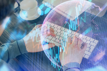 Double exposure of graph with man typing on computer in office on background. Concept of hard work.