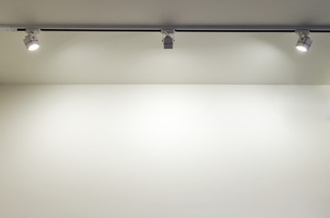 Light on a white wall. Three directional white lights located horizontally illuminate the empty wall of the residential interior from top to bottom.