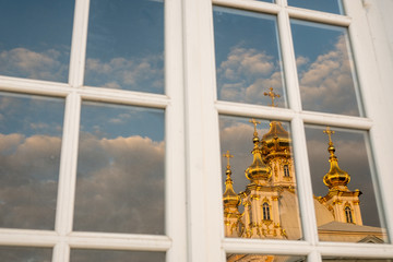 Reflection of the Orthodox Church in the window. Golden domes and crosses of the Grand Palace in Peterhof. Glitter of gold against the blue sky. Autumn sunny day.