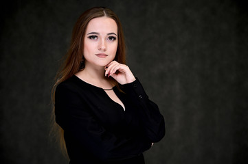 Portrait of a pretty brunette girl with beautiful hair, excellent make-up, beautiful face skin in a black blouse on a dark background. Made in the studio.