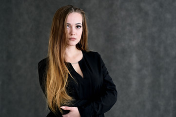 Portrait of a pretty brunette girl with beautiful hair, excellent make-up, beautiful face skin in a black blouse on a dark background. Made in the studio.