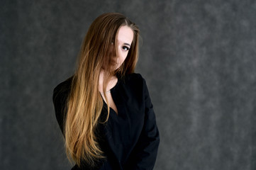 Portrait of a pretty brunette girl with beautiful hair, excellent make-up, beautiful face skin in a black blouse on a dark background. Made in the studio.