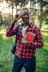 Obraz premium Black student in glasses holds book, summer park